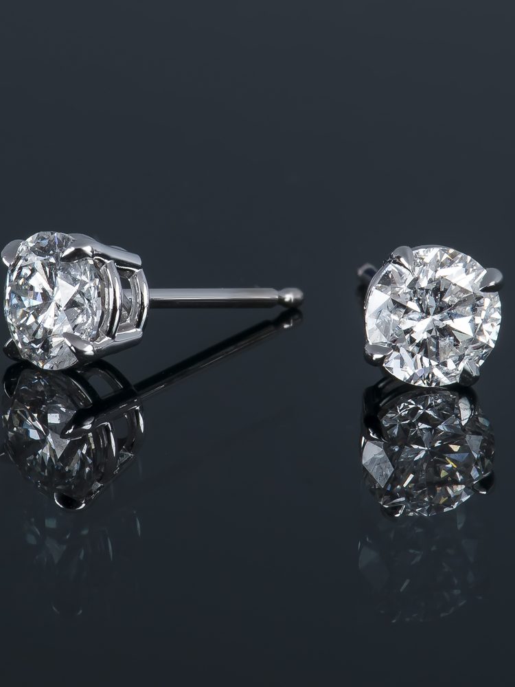 Two sparkling diamond stud earrings set in silver, reflecting light on a dark surface.